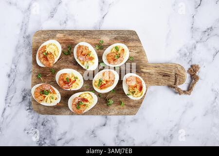 Gekochte Eier mit Eigelb gefüllt und mit Mayonnaise gewürzt, gefüllte Eier mit Garnelen, auf einem hölzernen Schneidebrett, selektive Fokussierung, Nahaufnahme, keine Leute Stockfoto