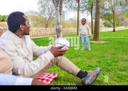 Vater und Sohn verbinden sich bei einem Ballspiel in einem sonnigen Park und genießen wertvolle Familienmomente zusammen Stockfoto