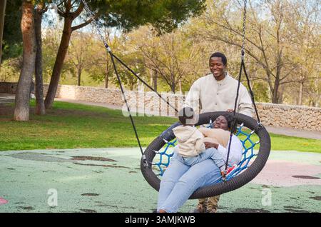Vater schiebt Mutter und Sohn auf eine Nestschaukel im Park und genießt eine gute Zeit zusammen Stockfoto