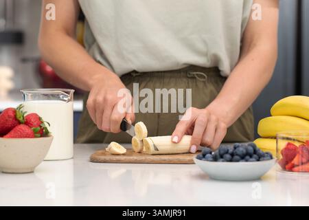Frau, die Bananen schneidet. Zubereitung eines gesunden Frühstücks mit frischem Obst und Milch Stockfoto