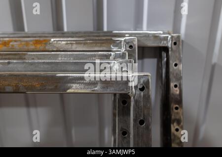 Mehrere geschweißte Metallrahmen mit gebohrten Löchern werden in einer Werkstattumgebung gegen eine gewellte Metallwand gestapelt. Stockfoto