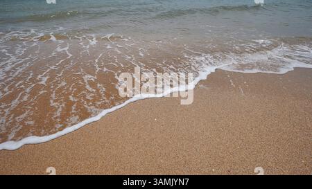 Sanfte Wellen, die über den goldenen Sand eines Strands auf der krim strömen, schaffen eine ruhige und friedliche Atmosphäre Stockfoto