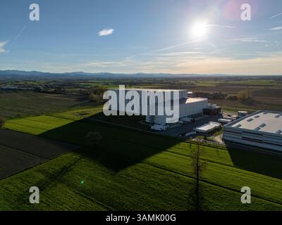 PC, Italien - 26. März 2025 - Automatisches Kühlhaus von oben betrachtet, Flurförderzeuge transportieren Ladung über grüne Landschaft, Schatten Stockfoto