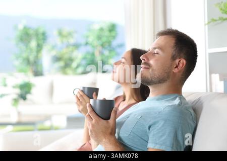 Ein Paar, das zu Hause auf einer Couch sitzt und Kaffee trinkt Stockfoto