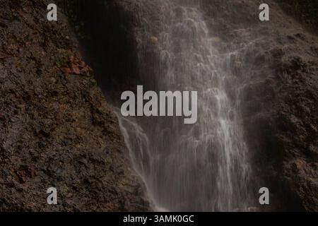 Nahaufnahme eines Wasserfalls, der über eine zerklüftete felsige Oberfläche im Wald stürzt Stockfoto
