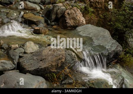 Kleiner Wasserfall über Felsen in einer friedlichen natürlichen Umgebung. Felsiges Gelände mit einem kleinen Wasserfall, der über große, glatte Steine kaskadiert. Stockfoto