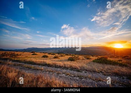 Sonnenuntergang beleuchtet Krim-Berge und Steppenlandschaft mit unbefestigtem Weg Stockfoto