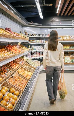Person, die eine lebhafte Auswahl an frischem Obst und Gemüse im Lebensmittelgeschäft durchstöbert. Eine Vielzahl von Produkten, die ordentlich in Regalen angeordnet sind, schafft ein einladendes Einkaufsumfeld Stockfoto
