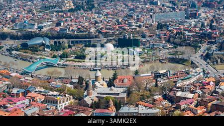 Ultra-weites Panorama auf Tiflis Stadt, das sich entlang des Flusses Kura erstreckt und Brücken, historische Viertel und Hügelbauten zeigt. Stockfoto