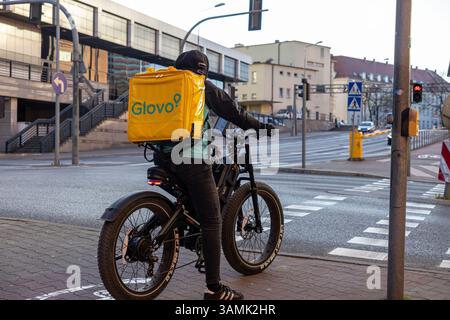 Posen, Polen - 8. April 2025: Kurier mit gelbem Glovo-Rucksack hält auf einem Elektrofahrrad an einem Straßenübergang der Stadt an und hebt auf App-basierte Lebensmittel-Delikatessen hervor Stockfoto