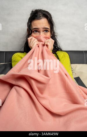 Eine verängstigte Frau, die ihr Gesicht mit rosa Decke bedeckt und Angst, Angst oder Stress erlebt Stockfoto