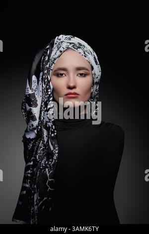 Die Frau zeigt einen auffälligen Ausdruck, während sie ein gemustertes schwarz-weißes Kopftuch trägt. Der Schwerpunkt liegt auf ihren Funktionen, die sanft gegen die Dunkelheit beleuchtet werden Stockfoto