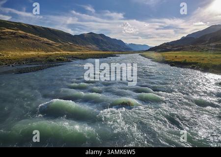 der fluss schlängelt sich anmutig durch ein Tal und spiegelt das lebendige Blau und Grün der Natur wider. Berge erheben sich majestätisch im Hintergrund und schaffen einen Stockfoto