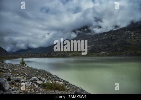 Der ruhige See spiegelt die Wolken darüber, umgeben von zerklüfteten Bergen in abgelegener Umgebung. Die felsige Küste trägt zur natürlichen Schönheit bei und weckt ein Gefühl von Stockfoto