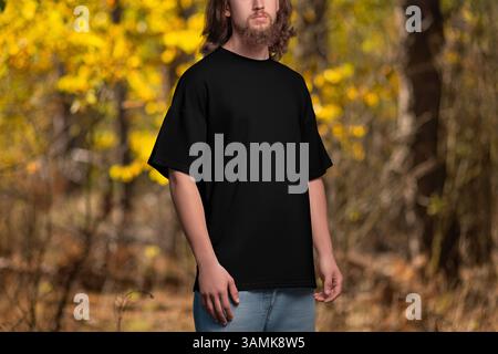 Mockup eines schwarzen übergroßen T-Shirts auf einem Mann mit langen Haaren, Bart, draußen, auf dem Hintergrund der Natur. Vorlage eines männlichen Freizeithemdes, Vorderansicht, Stockfoto