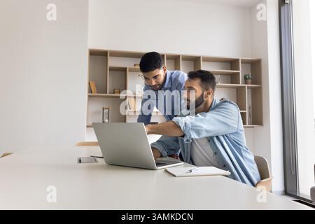 Erfahrener männlicher Büroangestellter der Millennials, der jüngere Kollegen am Arbeitsplatz ausbildet Stockfoto