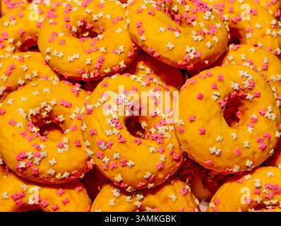 Nahaufnahme von gelb glasierten Donuts, verziert mit winzigen rosa und weißen Schmetterlingsstreuseln. Ein helles und fröhliches Dessert Stockfoto
