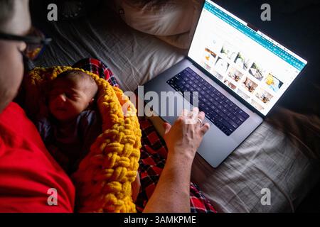 Vater hält Baby in der Hand, während er ein Notebook in Dim Light verwendet Stockfoto