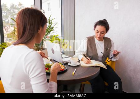 Brainstorming-Sitzung im Café mit zwei konzentrierten Weißen, die Ideen für Inhalte generieren. Konzept für kreatives Marketing und geschäftliche Bindung. Mitten im Shot. Stockfoto