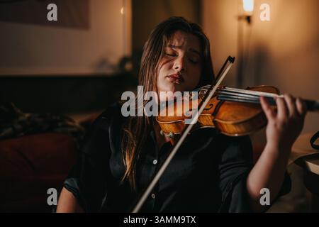 Frau spielt leidenschaftlich am Abend im schwach beleuchteten Raum Violine Stockfoto