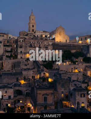 Blick aus der Vogelperspektive auf den Duomo di Matera bei Sonnenuntergang mit beleuchteten Dächern und historischer Architektur, Matera, Italien. Stockfoto