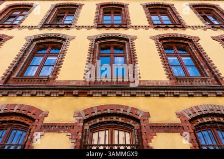 Traditionelle städtische Architektur mit hellgelb verputzten Wänden und braun-roten Ziegelfenstern, die bei Tageslicht kulturelle Details einfangen Stockfoto