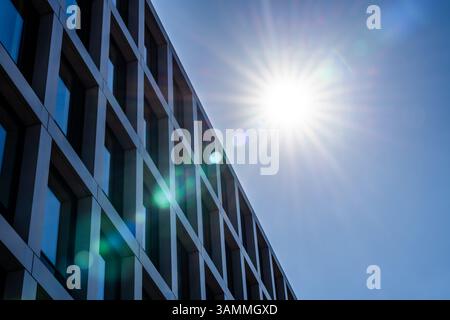 Modernes Bürogebäude unter voller Sonne mit strukturiertem Gitter aus Glasfenstern und klaren architektonischen Linien Stockfoto