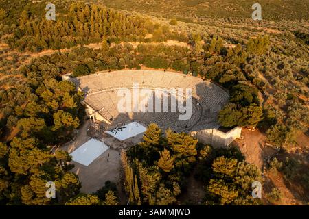 Blick aus der Vogelperspektive auf das antike Theater und Amphitheater umgeben von Bäumen in einer wunderschönen Landschaft, Asklipiio, Griechenland. Stockfoto
