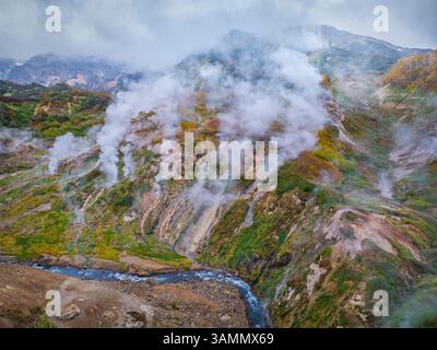 Blick aus der Vogelperspektive auf das atemberaubende Tal der Geysire mit dampfenden Geysiren und zerklüfteten Bergen, Kamtschatka, Russland. Stockfoto