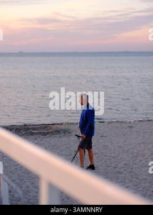 Malmö, Skåne, Schweden. August 2022. Mann, der abends am Strand von Ribersborg einen Metalldetektor benutzt. Stockfoto