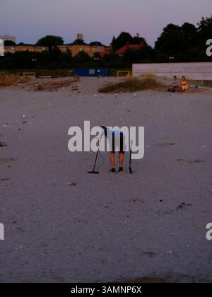 Malmö, Skåne, Schweden. August 2022. Mann, der abends am Strand von Ribersborg einen Metalldetektor benutzt. Stockfoto