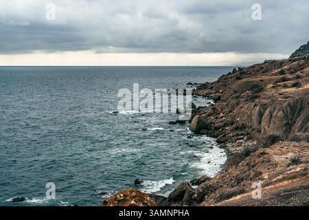 Blick auf die Küste mit felsiger Küste und bewölktem Himmel am Rand des Ozeans am späten Nachmittag Stockfoto