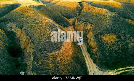 Geländefahrzeug durch zerklüftete Canyonlandschaften. Eine Luftaufnahme zeigt ein Geländefahrzeug, das auf einem schmalen, unbefestigten Pfad durch eine zerklüftete Schlucht fährt Stockfoto
