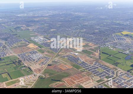 Blick aus der Vogelperspektive auf eine wunderschöne Wohngegend mit Feldern und Straßen unter bewölktem Himmel, Clyde North, Australien. Stockfoto