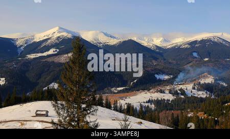 Snowy Mountain Village im Pine Forest Valley. Malerischer Blick auf ein abgelegenes Bergdorf, eingebettet in ein schneebedecktes Tal mit dichten Kiefernwäldern Stockfoto