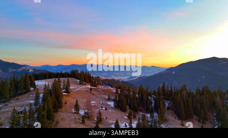 Malerischer Sonnenuntergang über einem bewaldeten Tal. Ein atemberaubender Blick aus der Vogelperspektive auf eine Berglandschaft bei Sonnenuntergang mit farbenfrohem Himmel und sanften Hügeln Stockfoto