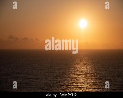 Ein atemberaubender Blick auf das Meer während der goldenen Stunde, mit warmen Orange- und Goldtönen, die sich vom ruhigen Wasser reflektieren. Die untergehende Sonne wirft eine friedliche gl Stockfoto