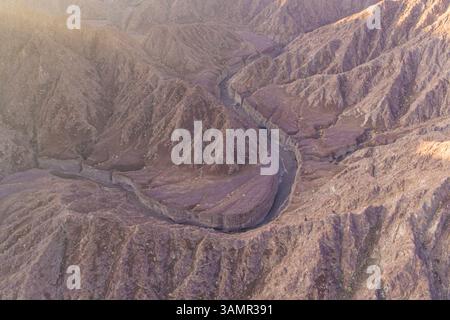 Aus der Vogelperspektive eines Canyons zwischen den felsigen und trockenen Bergen in der Wüste im Bundesstaat Ajman, Vereinigte Arabische Emirate. Stockfoto