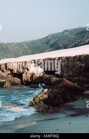 Am Delisha Beach, Socotra, prallen Wellen gegen die felsige Küste unter den Sanddünen. Stockfoto