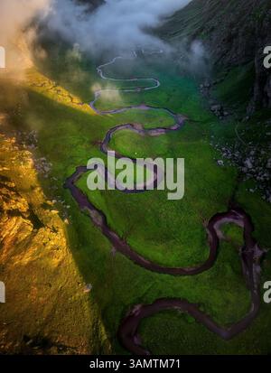 Aus der Vogelperspektive auf einen sich schlängelnden Fluss durch ein üppiges grünes Tal mit Bergen und Wolken, Aguas Tuertas, Huesca, Spanien. Stockfoto