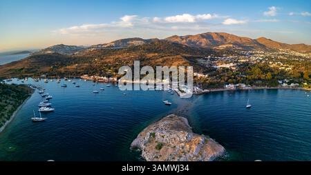Aus der Vogelperspektive auf Boote und Segelboote im türkisfarbenen Wasser mit malerischen Bergen und Dorf Gumusluk, Türkei. Stockfoto