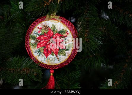 Kreuzgenähtes Weihnachtsschmuck auf einem Weihnachtsbaum. Dieses runde Weihnachtsschmuck mit Weihnachtsstern und Stickerei mit Wort Hoffnung Stockfoto