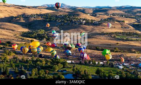 Aus der Vogelperspektive sehen Sie bunte Heißluftballons über einem malerischen Tal mit Bergen unter klarem Himmel, West University, Reno, Nevada, USA. Stockfoto