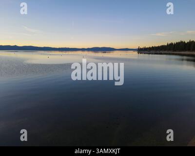 Blick aus der Vogelperspektive auf den ruhigen Winteruntergang über einem spiegelähnlichen See mit Reflektionen von fernen Hügeln und ruhigen Wäldern, Zephyr Cove, Nevada, USA. Stockfoto