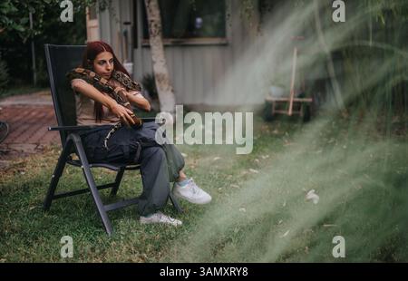 Ein Mädchen sitzt ruhig draußen mit einer großen Schlange auf den Schultern Stockfoto