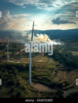 Luftaufnahme eines modernen Windparks mit einem Feuer im Hintergrund, Palermiti, Kalabrien, Italien. Stockfoto