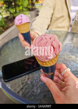 Zwei Hände halten zwei Eiskegel an einem Tisch im Freien und genießen einen sonnigen Tag Stockfoto