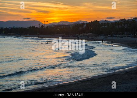 Ein orangefarbener Sonnenuntergang leuchtet am Himmel über Salou, Costa Dorada, Spanien mit Bergen und hohen Kranichen in der Ferne Stockfoto