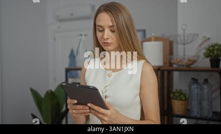 Frau, die im Büro mit Tablet arbeitet, umgeben von Pflanzen und moderner Einrichtung, die tagsüber einen beruhigenden professionellen Raum schafft. Stockfoto