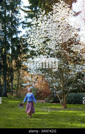 Frau, die sich fröhlich unter dem blühenden Magnolienbaum in einem Frühlingspark dreht Stockfoto